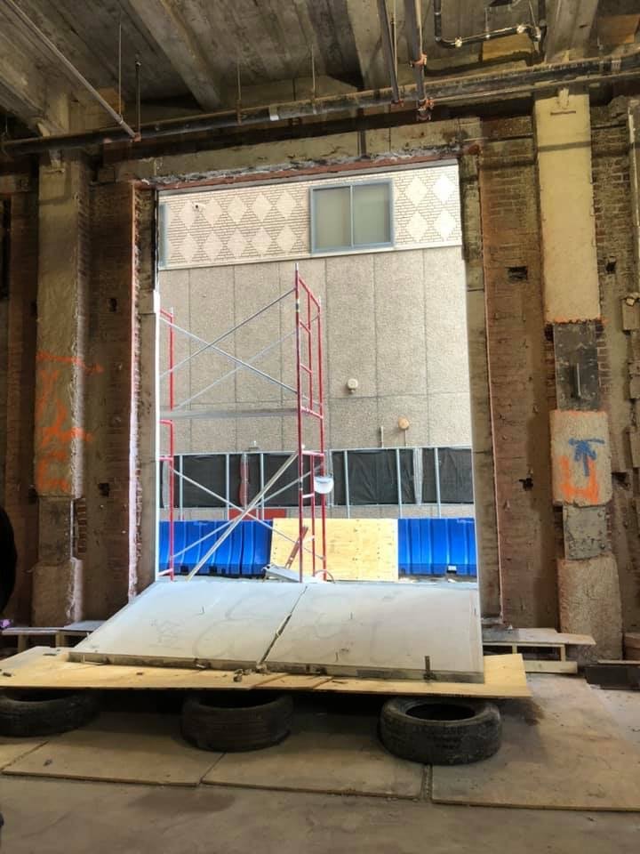 A large doorway under construction with a scaffold outside, a concrete slab on the ground, and exposed building materials visible.