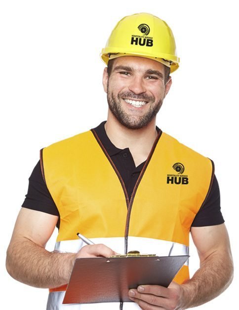 A man wearing a yellow hard hat and safety vest is smiling while holding a clipboard and pen.