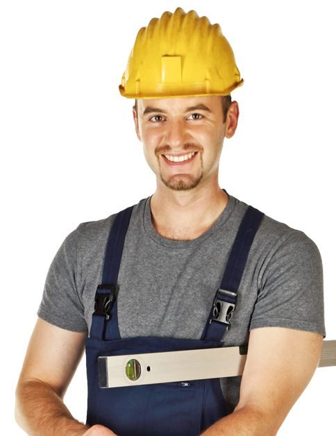 A man wearing a yellow hard hat and blue overalls holds a spirit level and smiles at the camera against a white background.