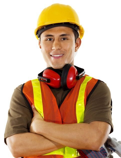 A construction worker wearing a yellow hard hat, orange safety vest, and red ear protectors stands with arms crossed, smiling at the camera.